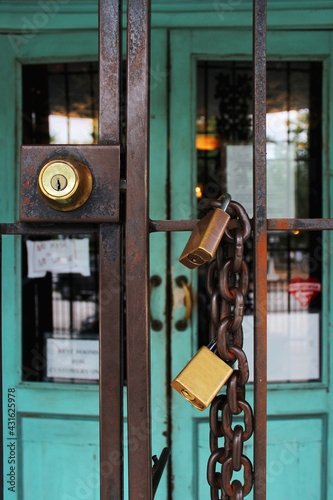 A keyhole and a padlock with a chain on the grate of a closed shop with a green door. A locked shop.