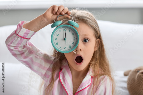 Stressed little girl with alarm clock in bed