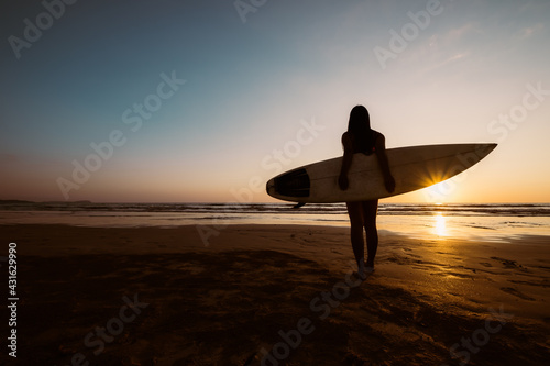 Silhouette of beautiful sexy surfer female with surfboard on the sandy beach at sunset. water sports. Surfing are healthy active lifestyle. Summertime vacation.
