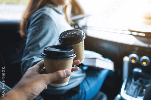 Closeup image of a young woman holding a map and clinking coffee cup with friend while riding in the car