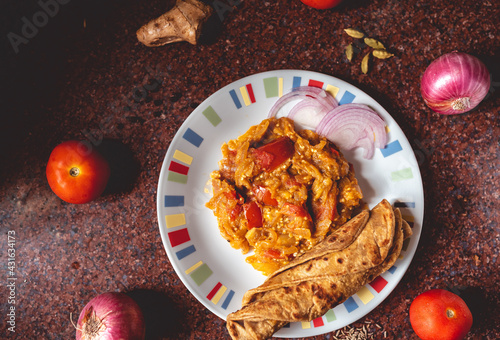 Freshly prepared eggplant in traditional spices served with Indian bread. Flat lay of north Indian spicy brinjal on a kitchen slab with fresh ingredients decorated around it. photo