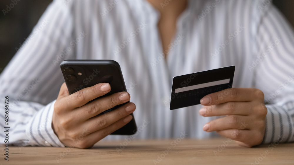 Close up woman paying online by credit card, using smartphone, sitting at wooden desk, young female holding phone, browsing banking service, checking balance, shopping, making internet payment Close up woman paying online by credit card, using smartphone, sitting at wooden desk, young female holding phone, browsing banking service, checking balance, shopping, making internet payment