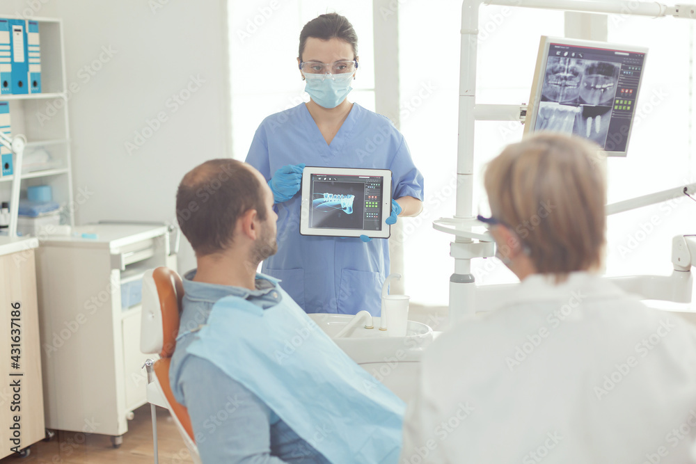 Medical assistant reviewing tooth x ray to sick patient explaining somatology treatment. Man waiting somatology examination while hospital team working together in modern stomatology clinic.