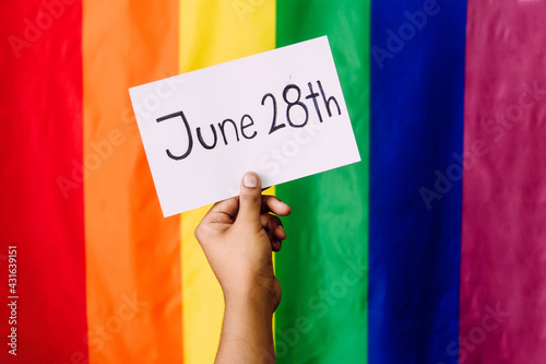 June 28th written on a piece of paper and held by a hand, international lgbt pride day, flag with rainbow colors in background