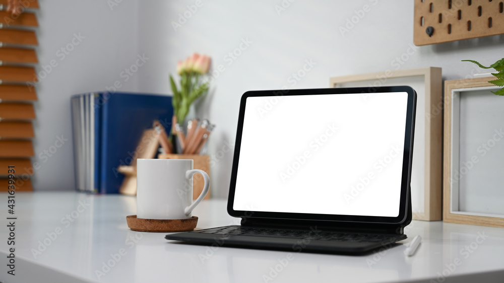 Mock up computer tablet with blank screen, coffee cup and supplies on white desk.