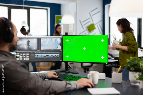 Videographer using computer with chroma key, mock up isolated display editing video and audio footage. Man editor processing film montage on pc with green screen while team working in background