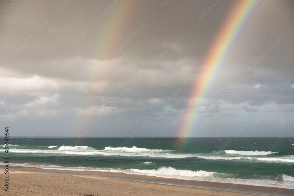 Double rainbow against grey clouds the the beach Double rainbow against grey clouds the the beach