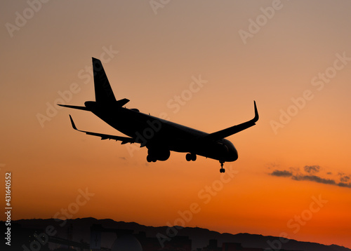 夕陽を背景に着陸態勢に入る飛行機のシルエット