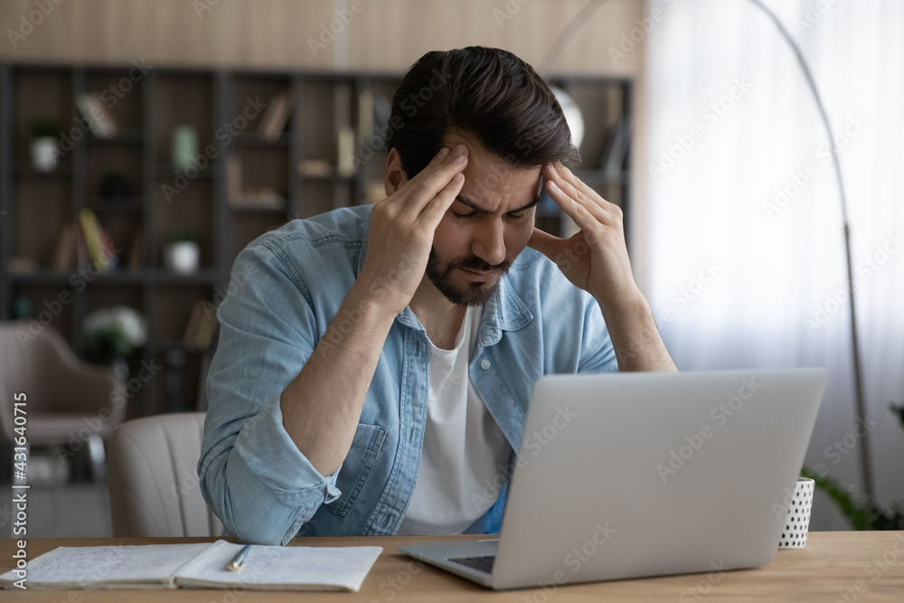Upset businessman with closed eyes touching massaging temples, suffering from strong headache or chronic migraine at workplace, sitting at desk with laptop, tired exhausted young man feeling pain Upset businessman with closed eyes touching massaging temples, suffering from strong headache or chronic migraine at workplace, sitting at desk with laptop, tired exhausted young man feeling pain