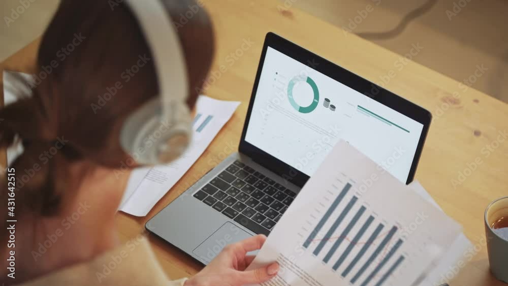 Female financial analyst on a remote work at home, working with documents and financial statements, view of infographics on laptop screen and documents, remote work in the context of a pandemic. Female financial analyst on a remote work at home, working with documents and financial statements, view of infographics on laptop screen and documents, remote work in the context of a pandemic.