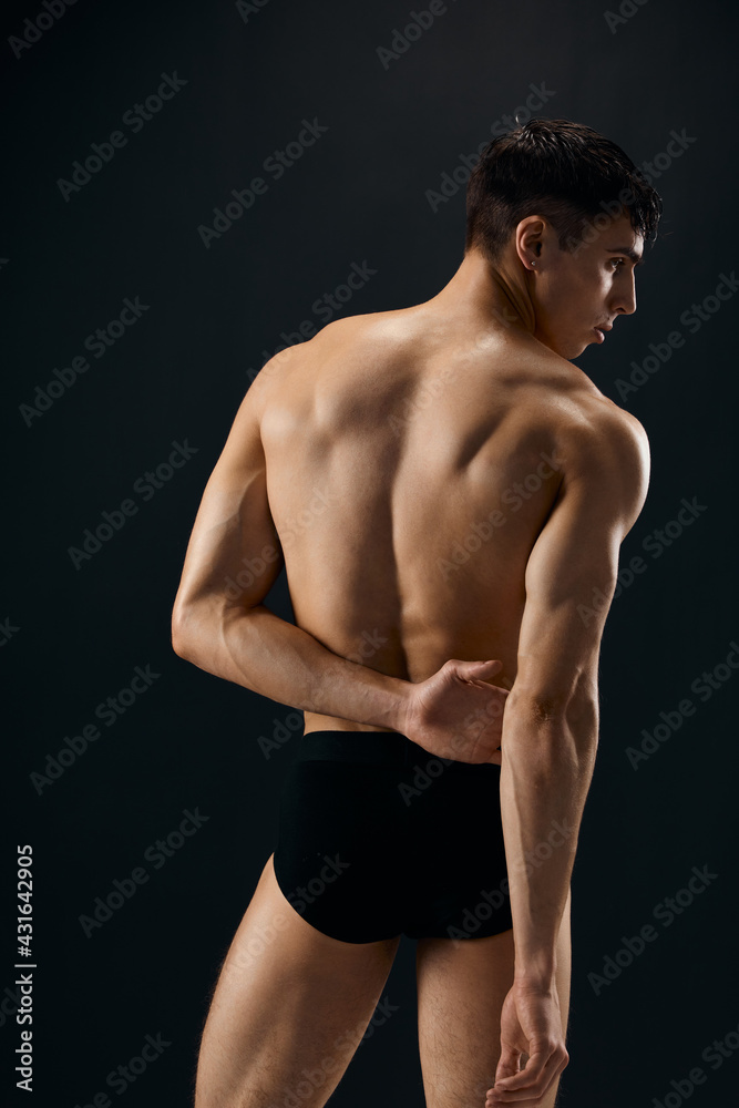 athletic man with a pumped-up body in dark shorts stands with his back