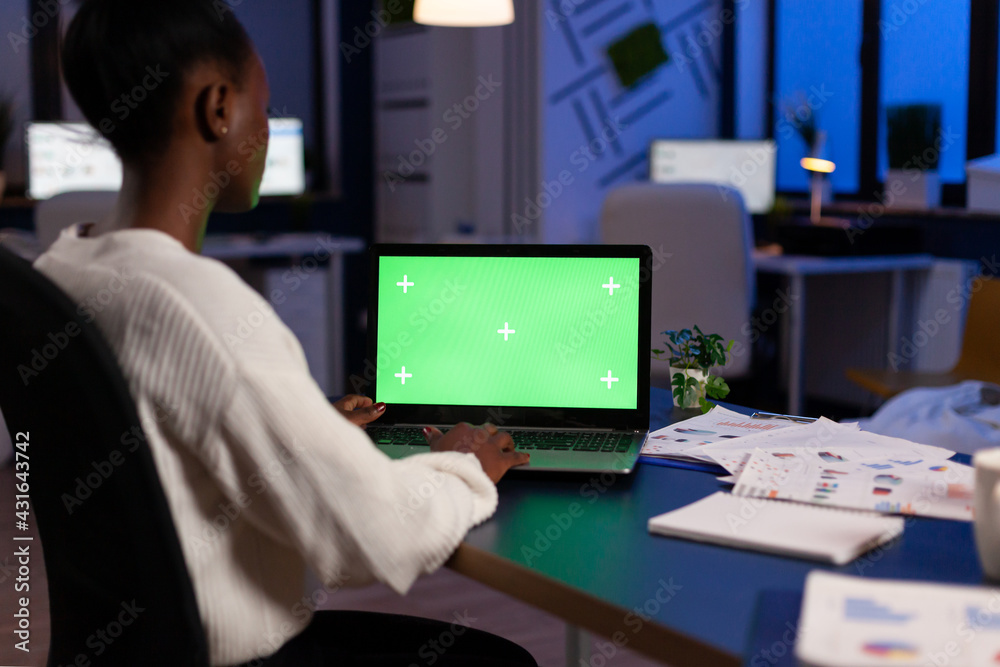 African manager typing at laptop with chroma key display during night time in start up business office working overtime. Freelancer watching mockup desktop monitor with green screen, writing data. African manager typing at laptop with chroma key display during night time in start up business office working overtime. Freelancer watching mockup desktop monitor with green screen, writing data.