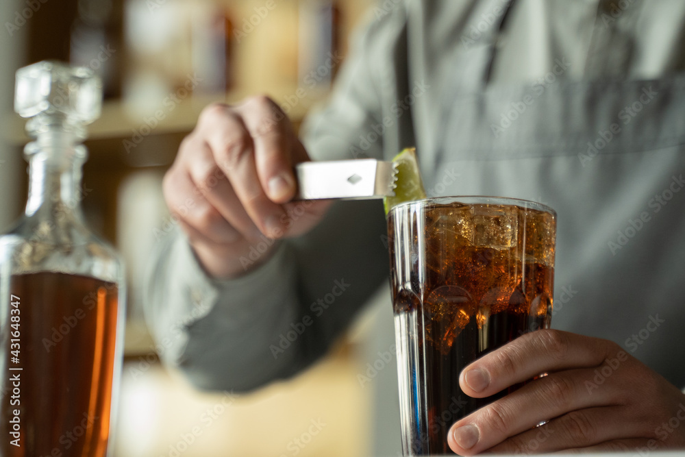 A professional bartender decorates the cocktail with lime. The bartender prepares a cocktail with whiskey and Cola. Preparing cocktails at the bar. A professional bartender decorates the cocktail with lime. The bartender prepares a cocktail with whiskey and Cola. Preparing cocktails at the bar.