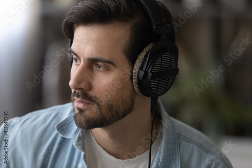 Close up head shot dreamy man wearing professional headphones looking to aside, listening to music, good sound quality, pensive musician artist dreaming about opportunities, visualizing future photo