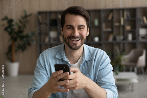 Head shot portrait laughing man holding smartphone, looking at camera, excited young male having fun with gadget, chatting in social networks with friends, satisfied customer shopping online