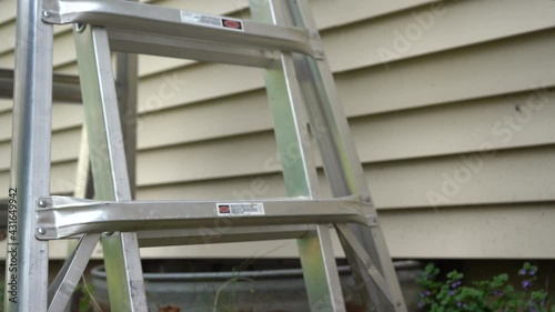 Construction ladder is placed in front of a rusted window well as worker climbs ladder.   photo