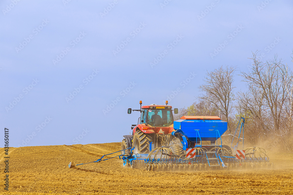 Obraz premium A farmer with a seeder on a tractor - sowing grain in an agricultural field. Growing wheat.