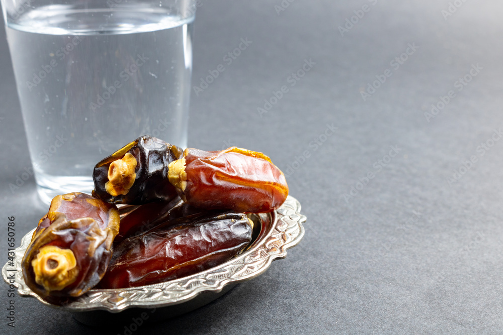 Selective focus of dates and a glass of water on gray background Selective focus of dates and a glass of water on gray background