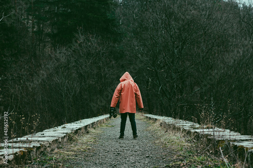 Man in orange hooded jacket with the mask in hand on the old abandoned stone railway viaduct.