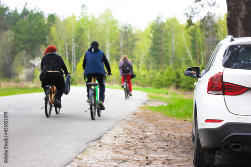 Fototapeta Naklejka Na Ścianę i Meble -  A white SUV car is parked on a side of a road. A concept of traveling by car, bicycles. Asphalt road in the woods. Back to normal life. Traveling short distances, exploring a surrounding countryside.