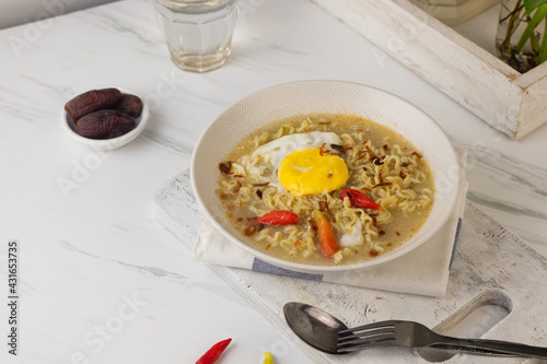 Mie Kuah Telur for Sahur in Ramadan, Instant noodle soup  served on white bowl with boiled pouch egg and chili.  White marble background. Copy space for text. 