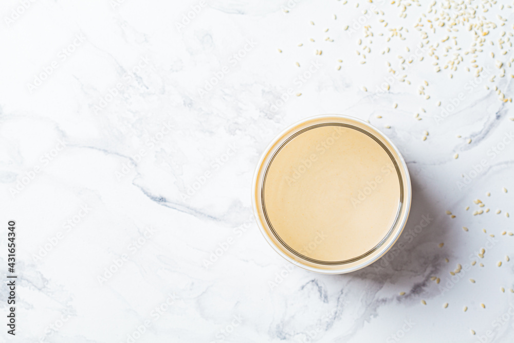 Sesame paste - tahini in glass jar, white marble background, top view. Israeli cuisine concept. Sesame paste - tahini in glass jar, white marble background, top view. Israeli cuisine concept.