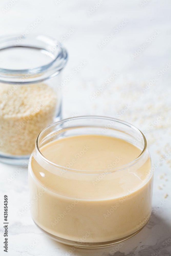 Closeup of sesame paste - tahini in glass jar, white marble background. Israeli cuisine concept. Closeup of sesame paste - tahini in glass jar, white marble background. Israeli cuisine concept.