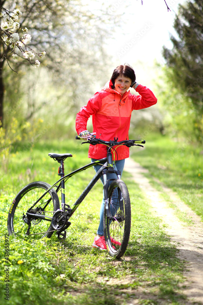 Beautiful woman on a bike in a blooming spring garden. Beautiful mature woman posing for the camera in a blooming spring garden. 