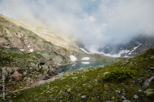 rocky shore of a mountain lake with turquoise water in dense fog and a high mountain in the background