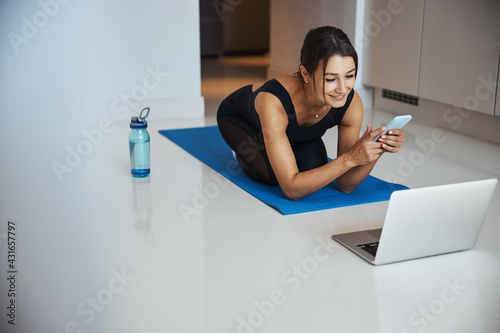 Cheerful sporty woman using cellphone and laptop at home