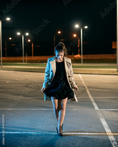 Girl in a coat in the parking lot against the backdrop of the night city with lanterns photo