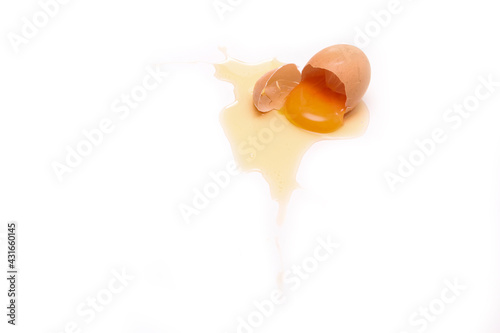 The fallen organic egg lies broken with the eggshell smashed and yolk and white flowing out of it. 