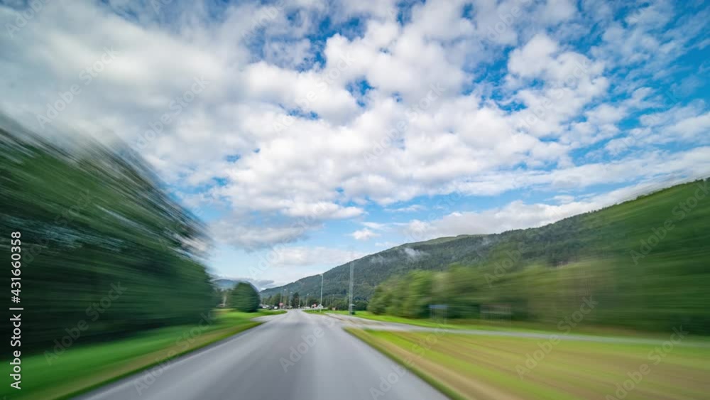A drive along the country road 65, in the valley of the Surna river, Norway. Two-lane freeway going through the lush landscape. Green farm fields and trees. Small towns and villages fly by. A drive along the country road 65, in the valley of the Surna river, Norway. Two-lane freeway going through the lush landscape. Green farm fields and trees. Small towns and villages fly by.