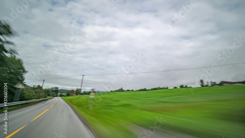 A road trip along the country road 65, in the valley of the Surna river, Norway. Two-lane freeway going through the lush landscape.  Green farm fields and trees. Small towns and villages fly by. photo