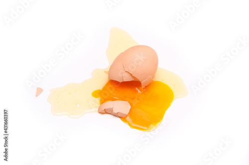 The fallen organic egg lies broken with the eggshell smashed and yolk and white flowing out of it. 