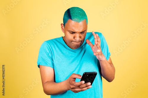 Black african man in casual on yellow background with mobile phone looks angry and outraged © Анастасия Каргаполов