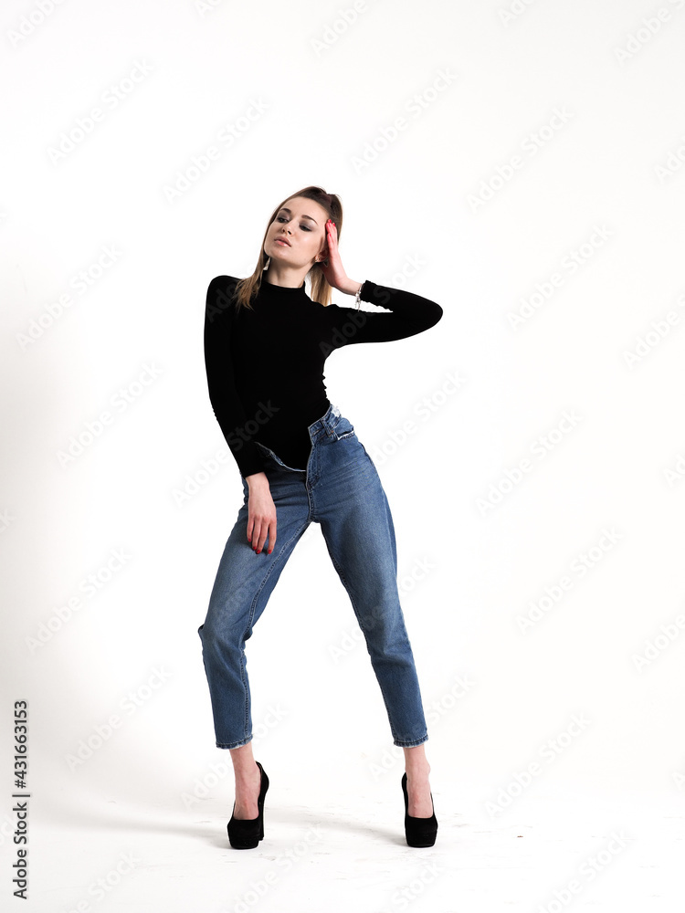 The brunette stands on a white background in a black bodysuit, jeans and high heels The brunette stands on a white background in a black bodysuit, jeans and high heels