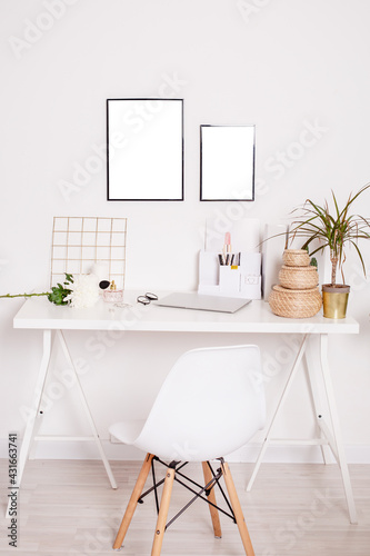 Accessories on shelf next to white chair at desk with laptop computer  plant and flowers in bright workspace
