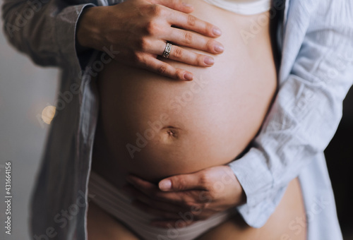 A pregnant girl gently holds a big belly with her hands close-up. Photography, concept. 