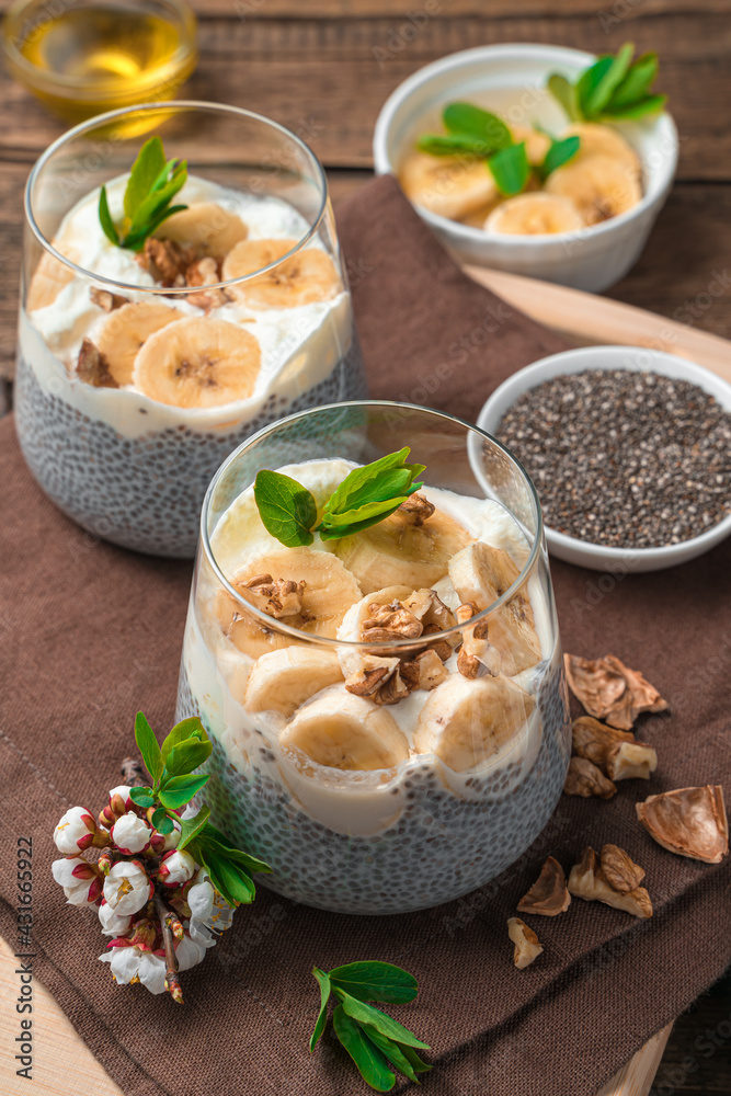 Two servings of healthy natural dessert with chia seeds on vegetable milk with banana, nuts and honey on a brown, wooden background. Side view, vertical.