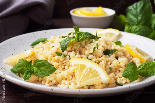 Boiled bulgur with fresh lemon and mint on a plate. A traditional oriental dish called Tabouleh. dark wooden background.