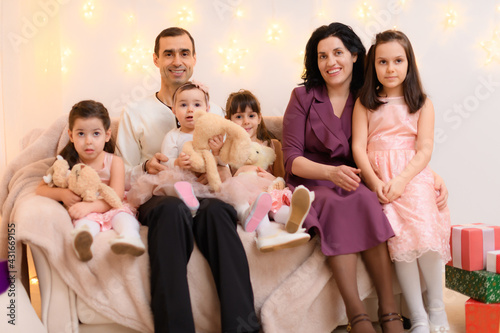 family portrait of a parents and children, sitting on a couch in home interior decorated with lights