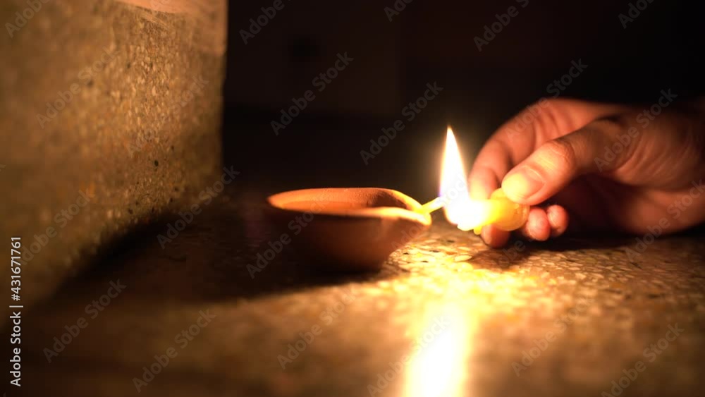 Hands lighting an oil clay candle diya on fire in a dark room on diwali festival, the holy festival of lights of India