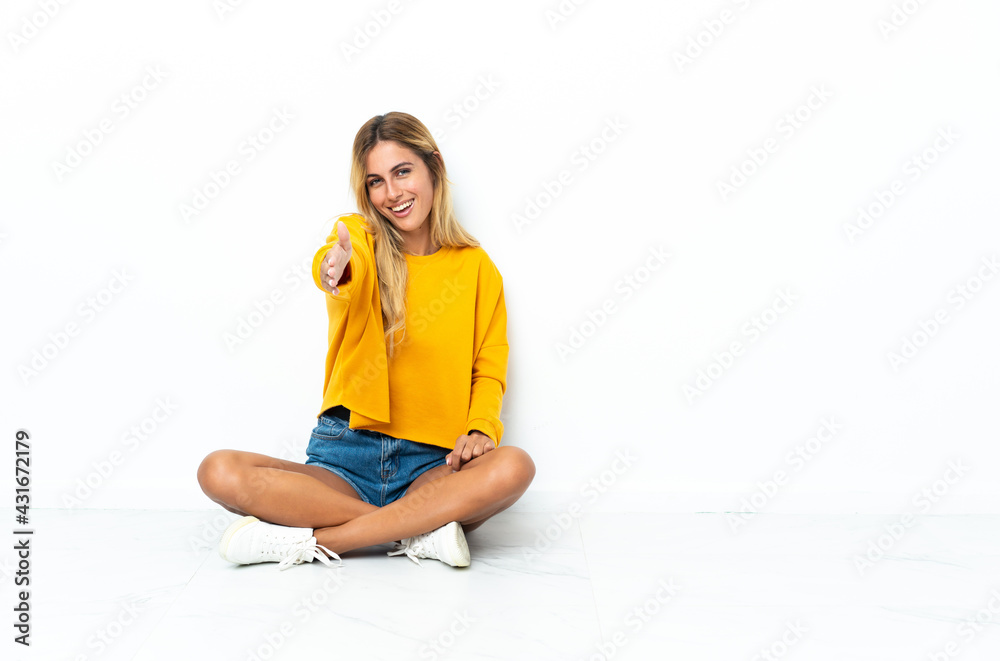 Young blonde Uruguayan woman sitting on the floor isolated on white background shaking hands for closing a good deal Young blonde Uruguayan woman sitting on the floor isolated on white background shaking hands for closing a good deal