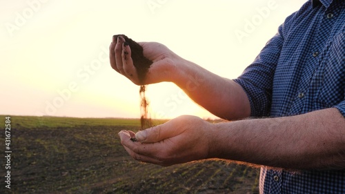 In hands of farmer, he holds handful of fertile land in sunshine on field in spring. Agriculture, agribusiness. In palms of gardener holds and pours humus, fertilized soil. Agriculture and fertility. photo