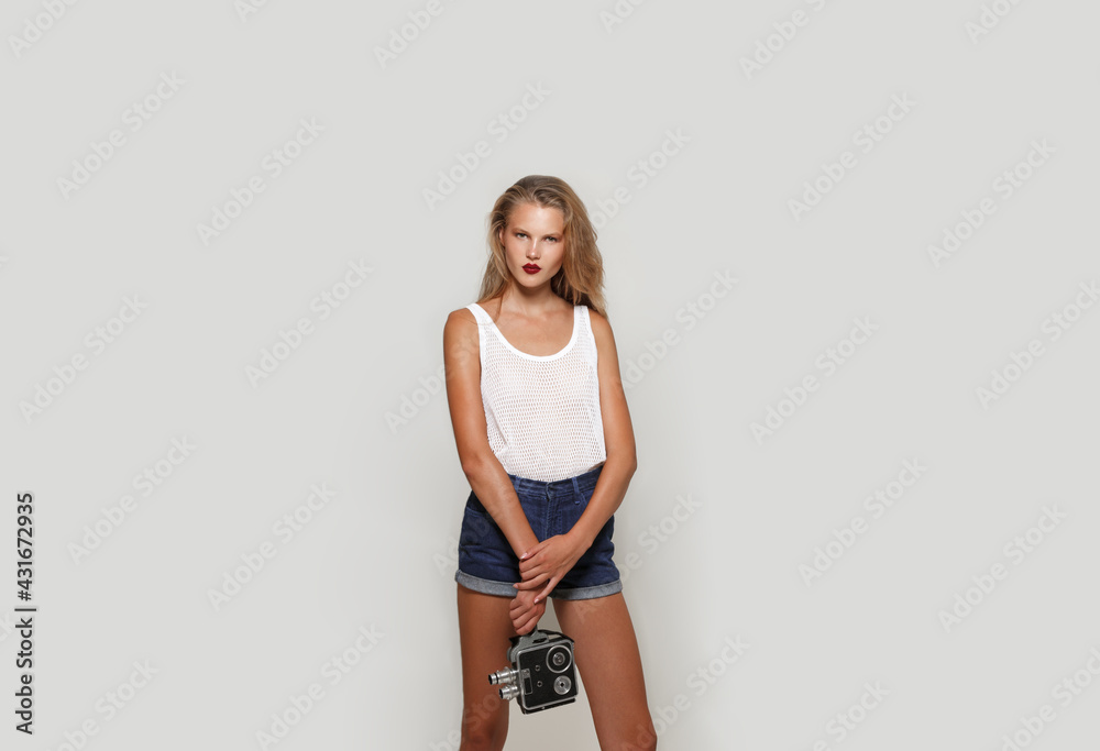 Attractive young blonde girl with make-up, holding in hands a retro camera, looking at camera, isolated over white background. Horizontal view. Attractive young blonde girl with make-up, holding in hands a retro camera, looking at camera, isolated over white background. Horizontal view.
