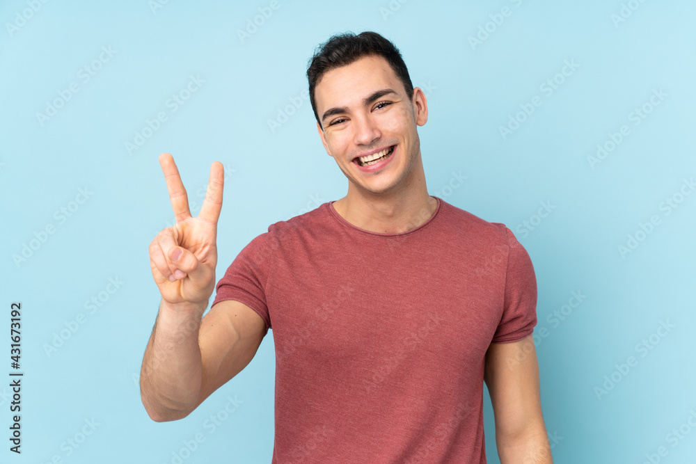 Young caucasian handsome man isolated on blue background smiling and showing victory sign Young caucasian handsome man isolated on blue background smiling and showing victory sign