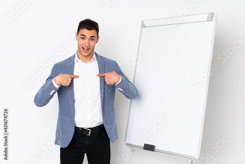 Young caucasian handsome man isolated on purple background giving a presentation on white board and with surprise expression photo