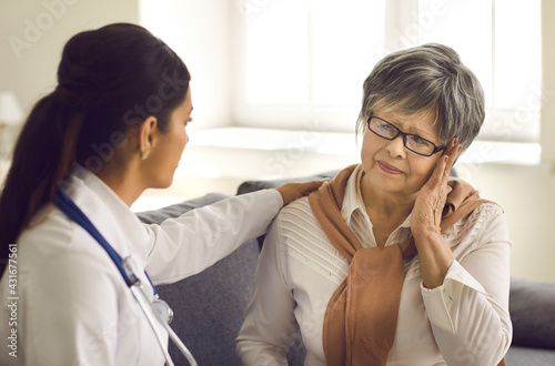 Mature woman telling doctor about pains and severe headaches during home visit or health checkup at hospital. Medical specialist helping older female patient who is suffering from stress and weakness