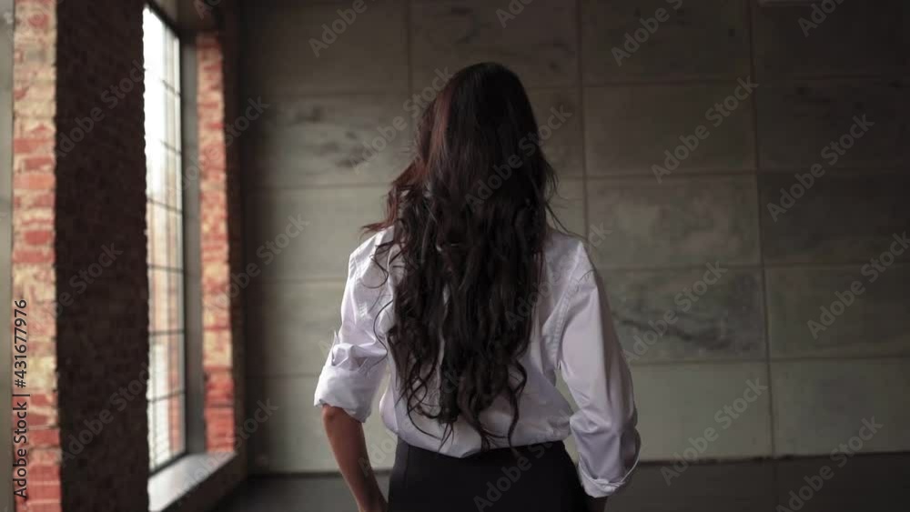 Unrecognizable brunette business woman in a white shirt walks through the office. Successful lady from the back. Slow motion. Unrecognizable brunette business woman in a white shirt walks through the office. Successful lady from the back. Slow motion.